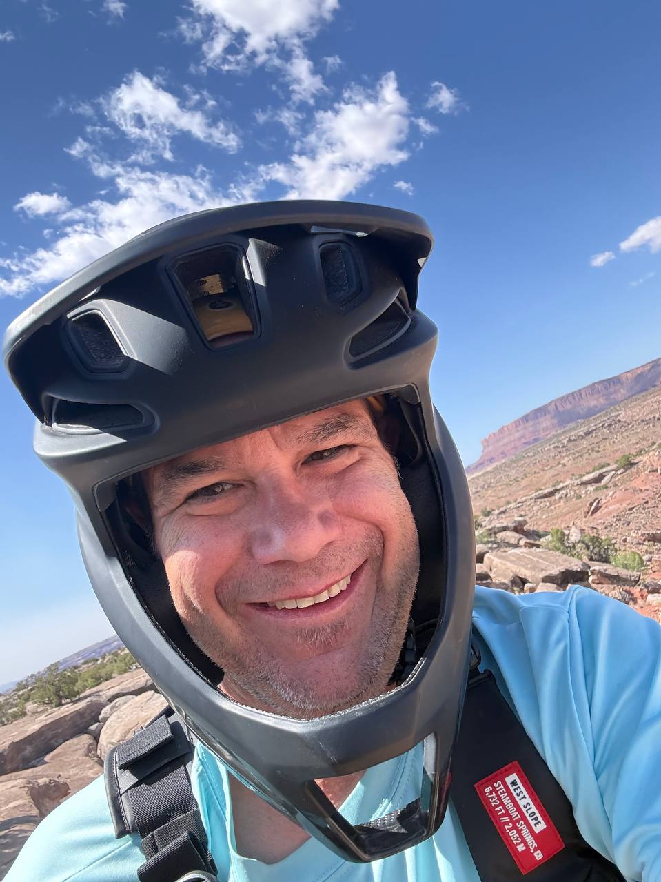 Shawn smiling in a full-face mountain bike helmet with desert canyon terrain behind him